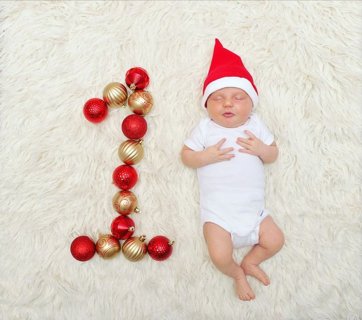 a baby laying next to christmas ornaments on a white rug