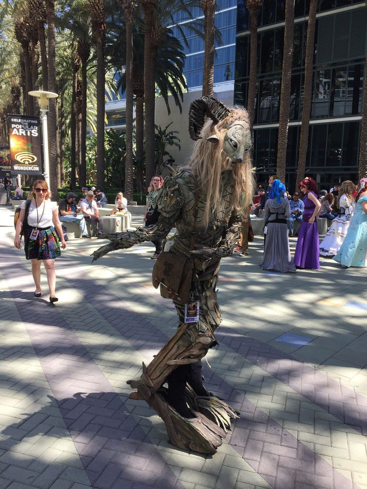 a costumed man dressed as a creature in the middle of a street with people walking by