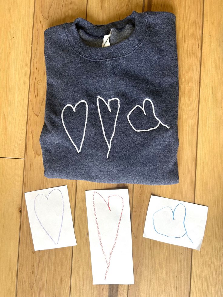 three t - shirts with hearts drawn on them sitting next to two pieces of paper