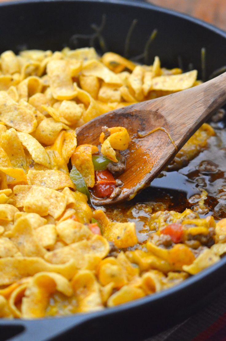 a skillet filled with tortilla shells and sauce being stirred by a wooden spoon