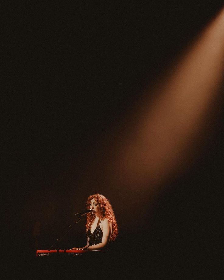 a woman with long red hair sitting at a keyboard in front of a microphone on stage