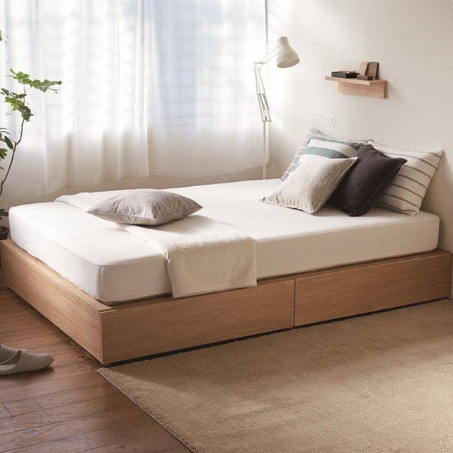 a bed sitting next to a window on top of a wooden floor in a bedroom