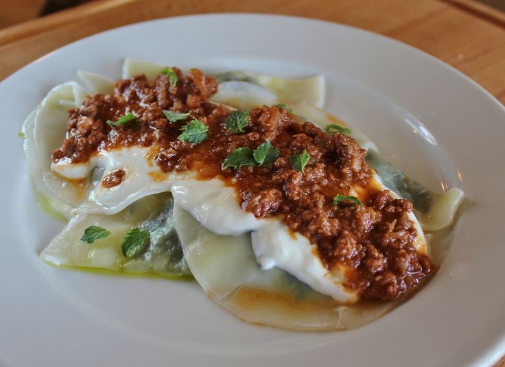 a white plate topped with dumplings covered in sauce and toppings on top of it