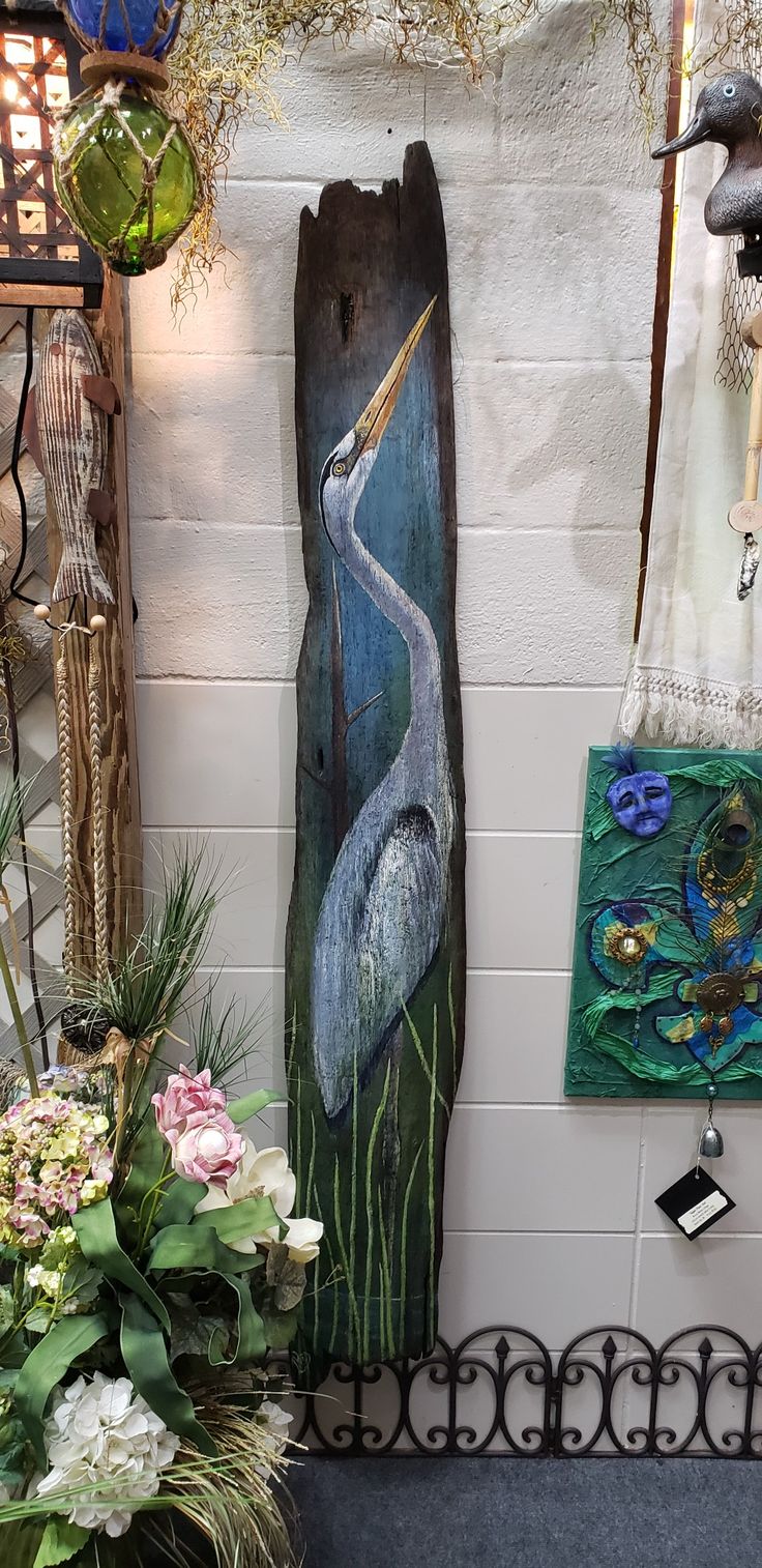 a painting of a bird is hanging on the wall next to some flowers and plants