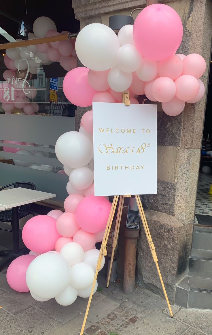 a welcome sign with pink and white balloons