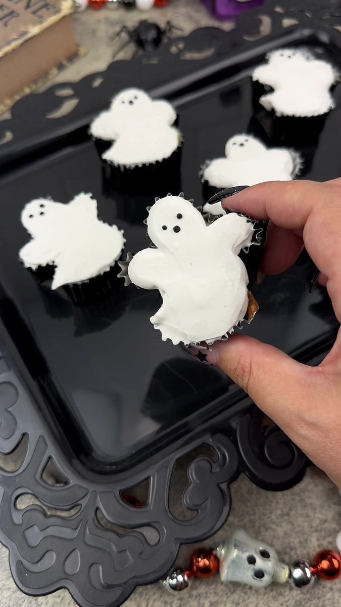 someone is decorating cupcakes with white frosting and ghost decorations on them