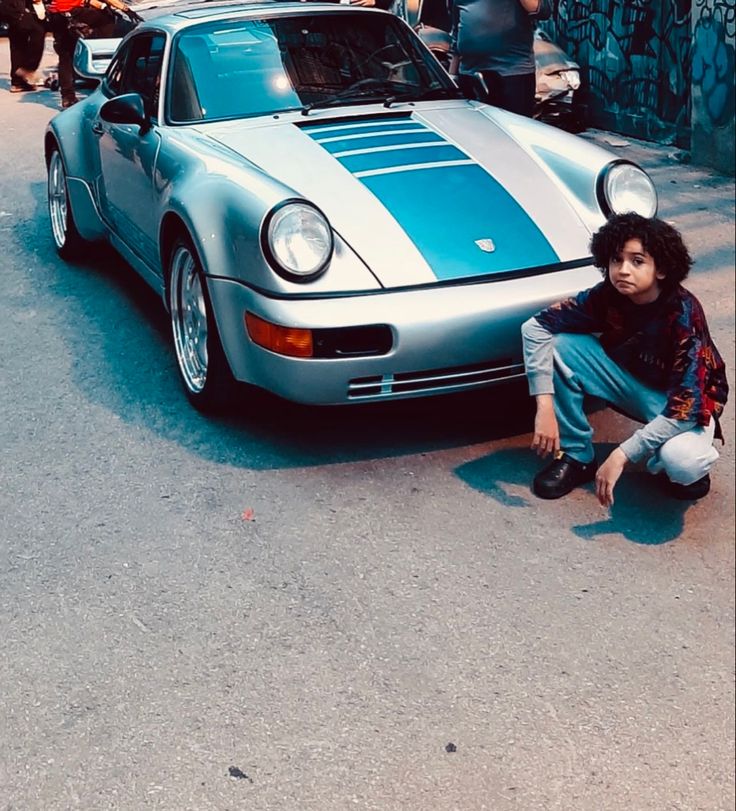 a man kneeling down next to a blue and white sports car