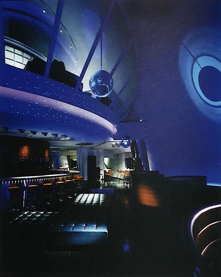 the interior of a restaurant with blue lighting and round lights hanging from the ceiling above it