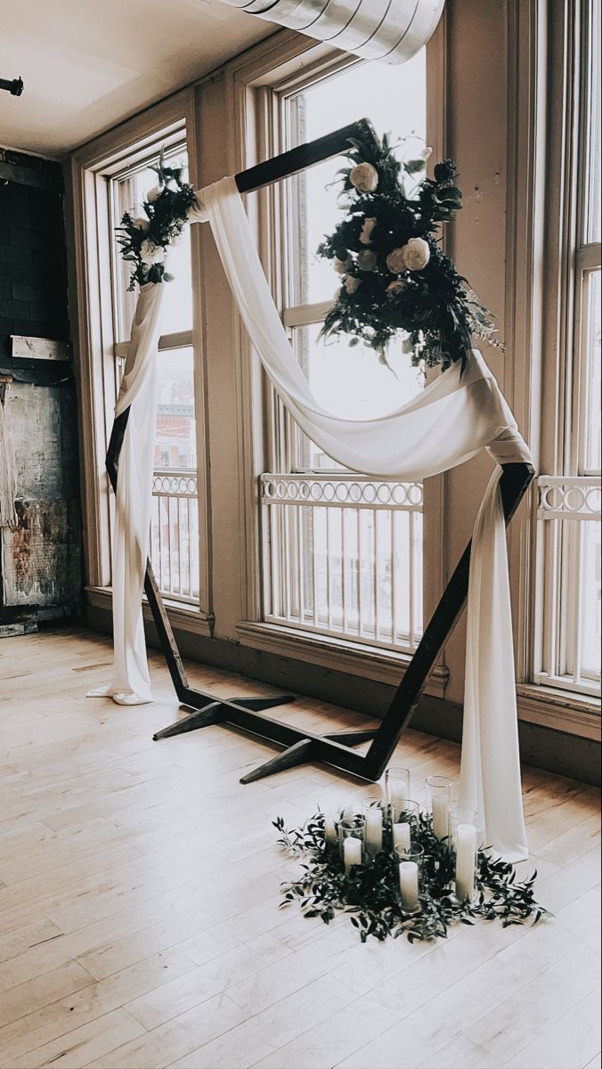 an arch decorated with flowers and candles in front of two large windows on the floor