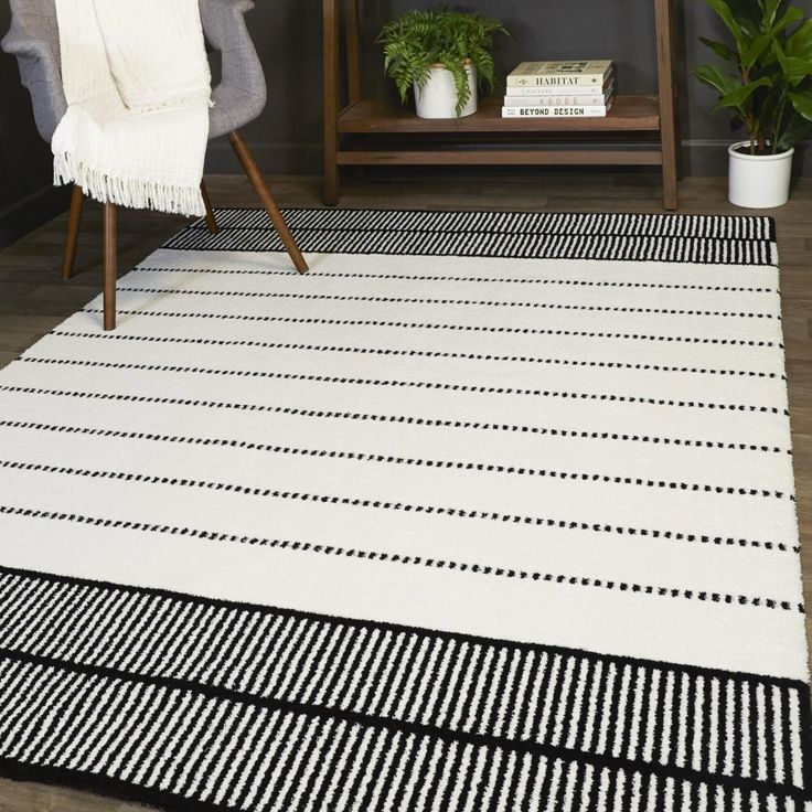 a black and white area rug in a living room with a chair, potted plant and bookshelf