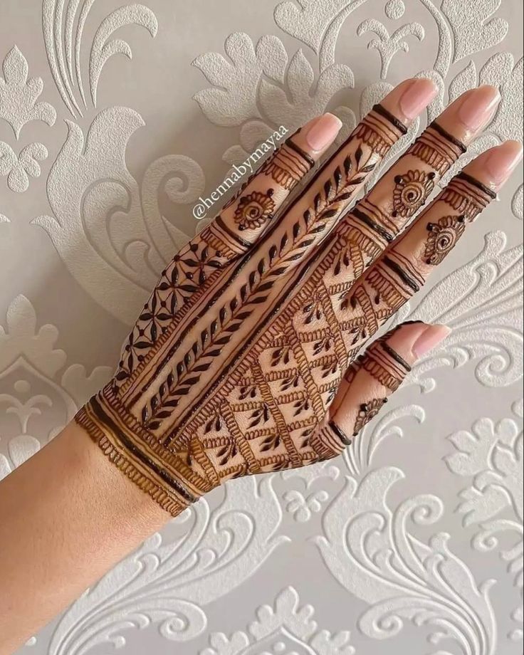 a woman's hand with hennap and intricate designs on the palm, against a wallpapered background