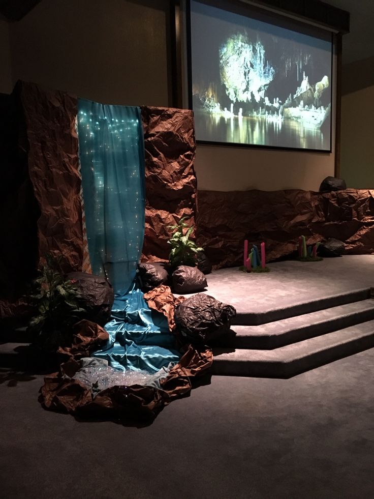 an empty stage with steps leading up to a projector screen in the background and rocks on the floor