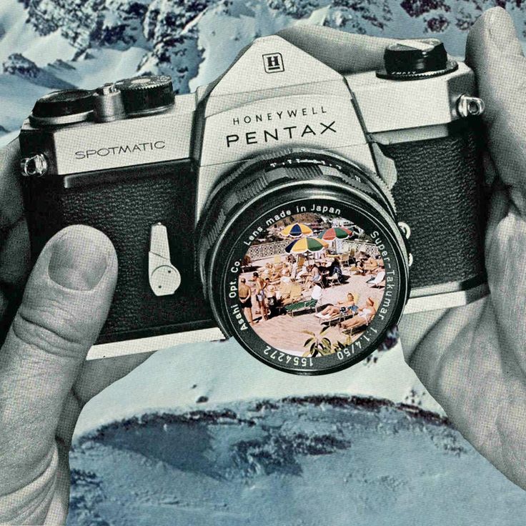 a person holding up an old camera in front of snow covered mountains