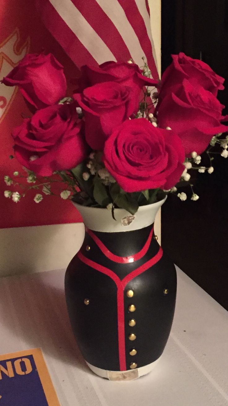 a black and white vase with red roses in it sitting on a table next to an american flag