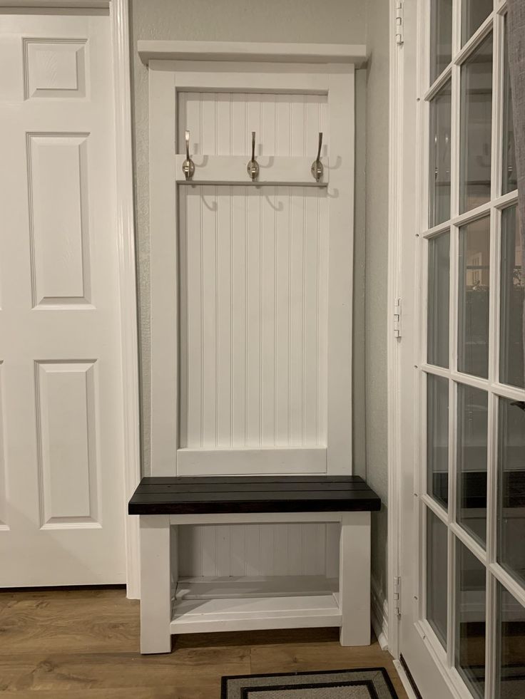 a white entryway with a bench and hooks on the wall next to glass doors