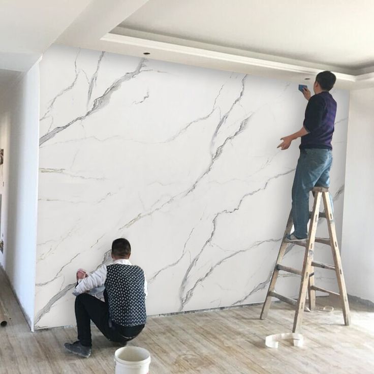 two men are working on a white marble wall in an empty room with ladders