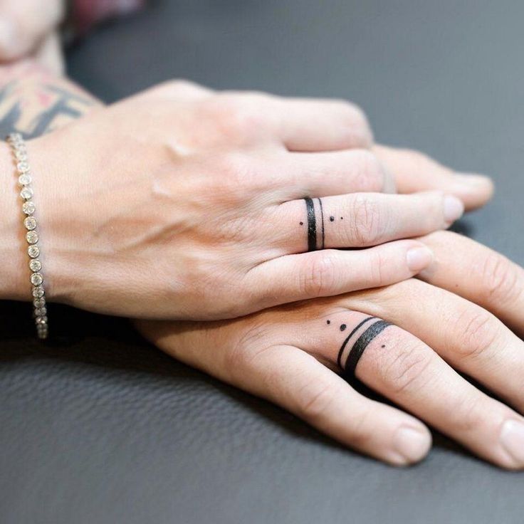 two people holding hands with tattoos on their fingers, one has a ring and the other has a finger tattoo