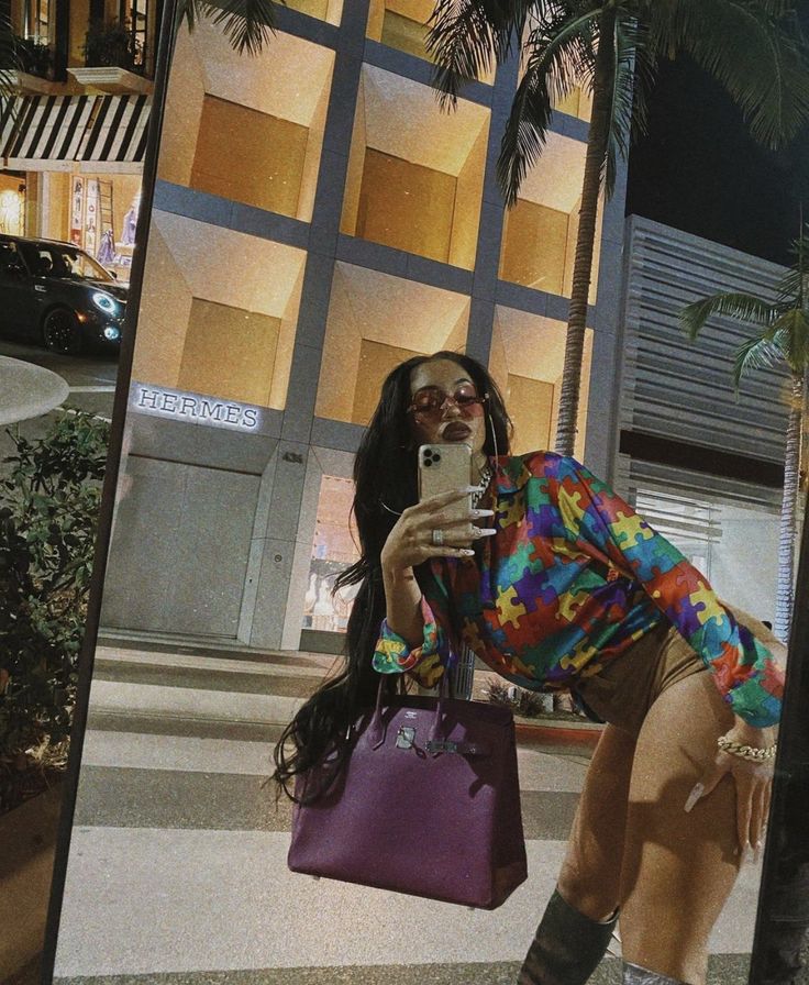 a woman taking a selfie in front of a tall building at night with her cell phone