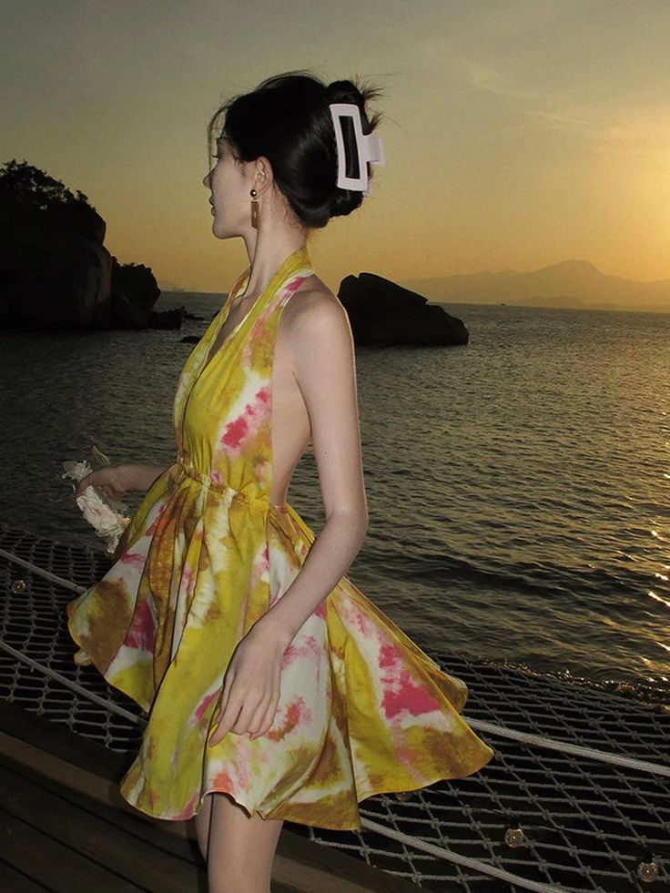 a woman in a yellow dress is standing on a dock near the water at sunset