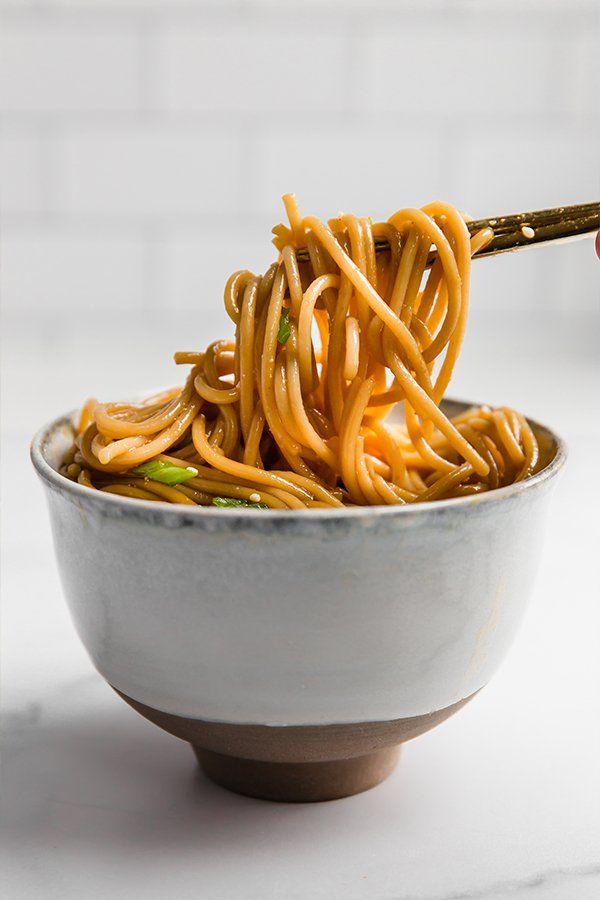 someone is holding chopsticks over a bowl of noodles