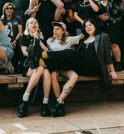 a group of people sitting on top of a wooden bench next to each other in front of a crowd