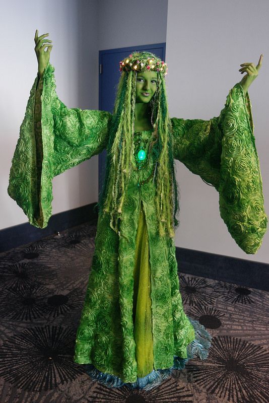 a woman dressed in green is holding up her hands and wearing a costume made out of grass