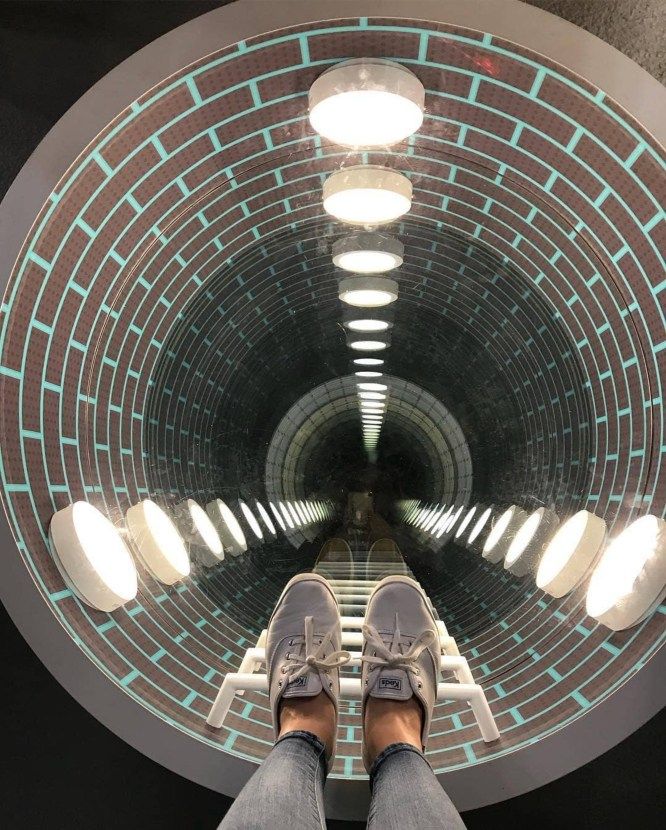 a person standing in front of a circular mirror with their feet on the ground and lights above them