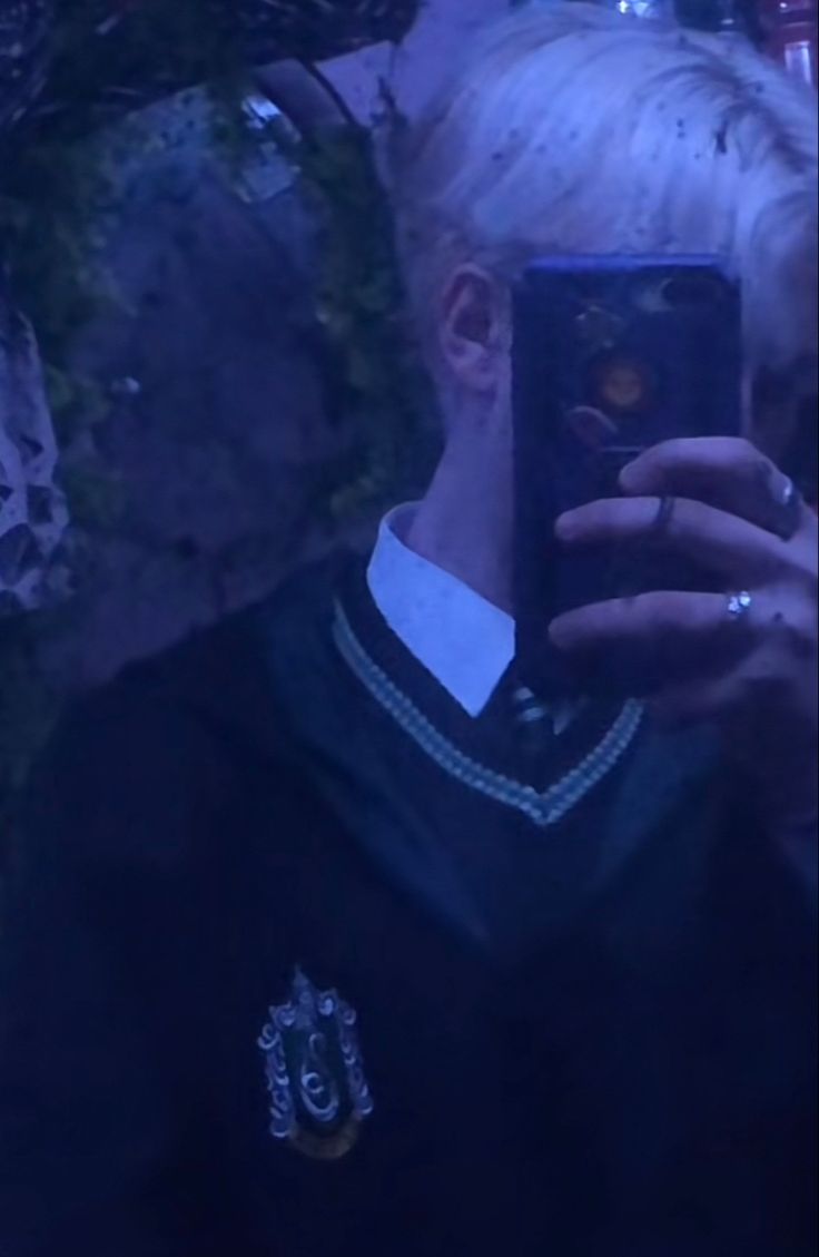 a man with blonde hair taking a selfie in front of a mirror wearing a harry potter sweater