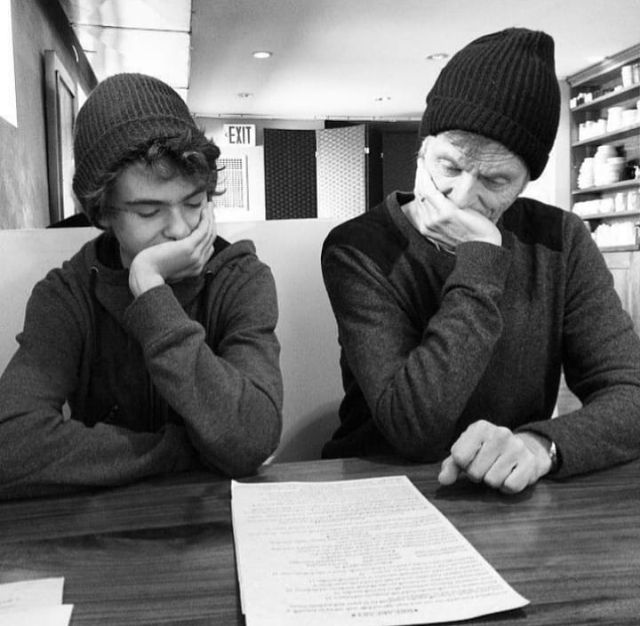 two men sitting at a table with papers and pens in front of them, both wearing beanies