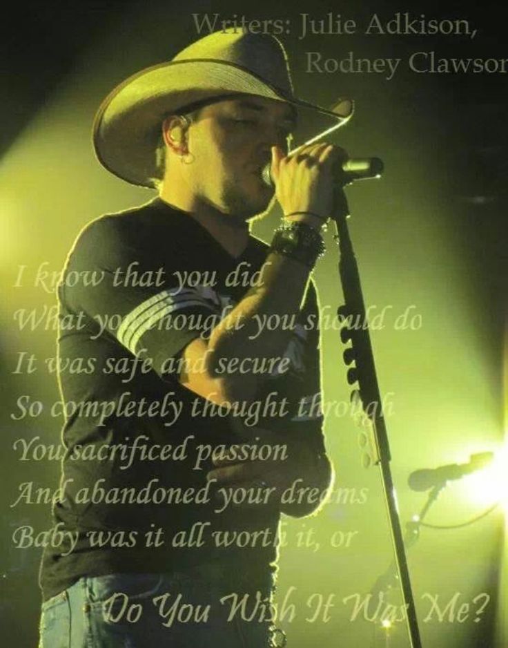 a man wearing a cowboy hat and holding a microphone in front of a stage with words written on it