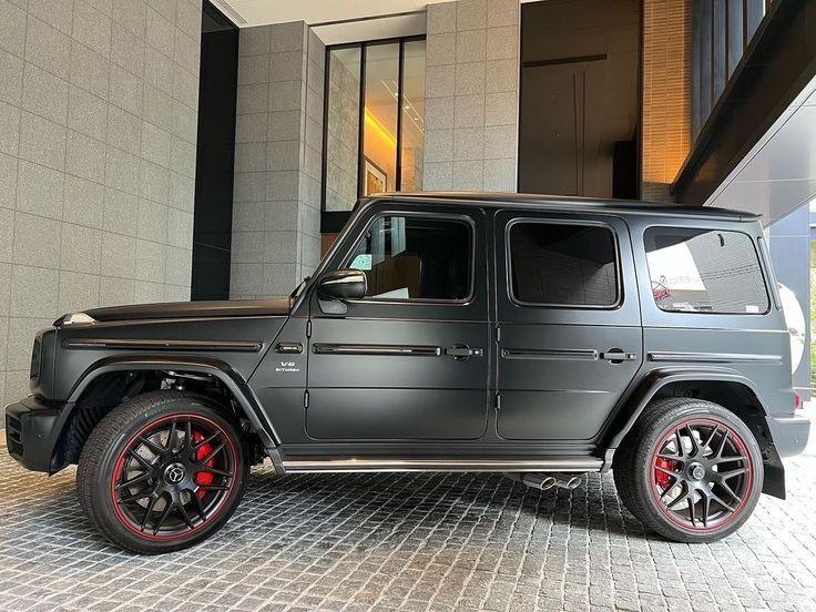 a black mercedes g - class is parked in front of a building with red rims