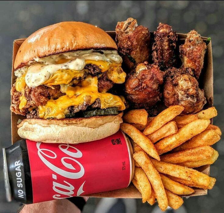 a person holding up a box of food with chicken and cheese on it next to french fries