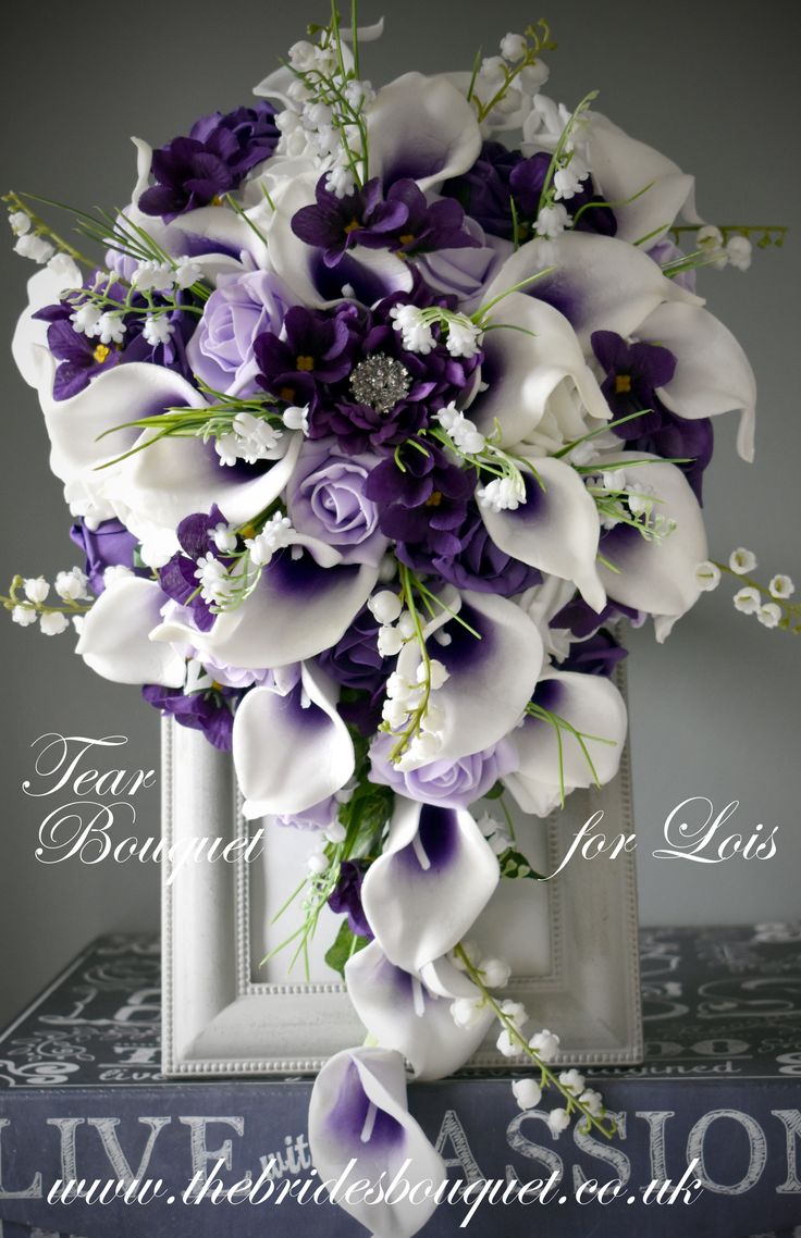 a bouquet of purple and white flowers on top of a table with an ornate frame