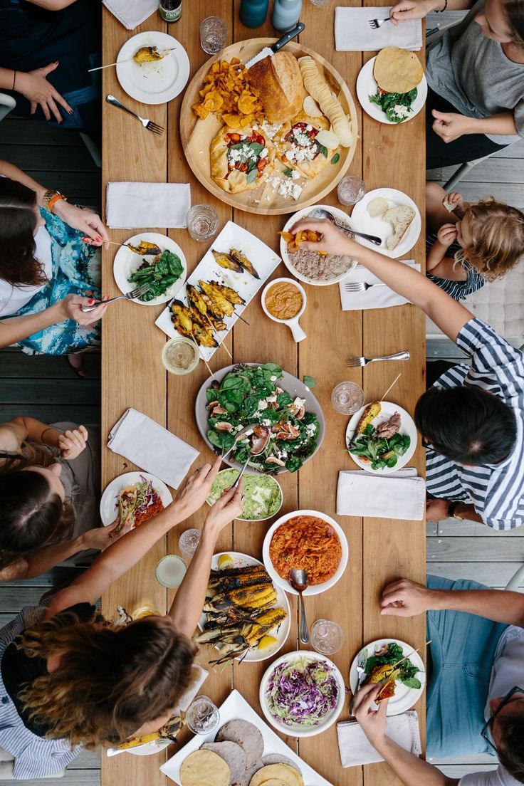 several people sitting at a table with plates and bowls of food in front of them