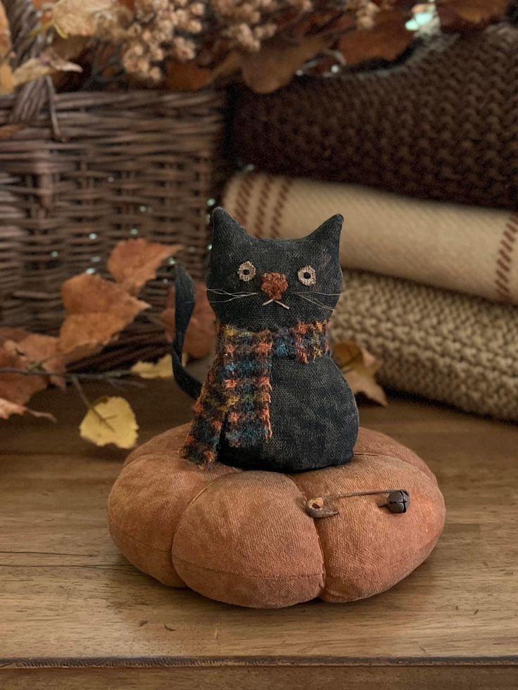 a black cat figurine sitting on top of a pumpkin shaped rock in front of fall leaves