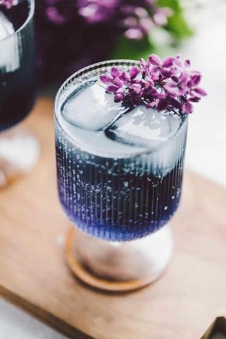 two glasses filled with purple flowers on top of a wooden tray next to each other