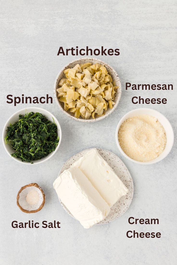 ingredients to make an artichoke recipe laid out in bowls on a white surface