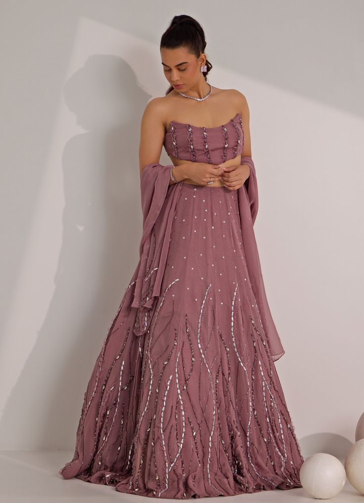 Elevate your style effortlessly with the striking Lilac Embellished Lehenga with Corset Blouse, designed to make a lasting impression. Crafted from luxurious organza, the Lilac flowing lehenga features intricate mix-media embroidery, creating a delicate shimmer with silver embellishments that add an ethereal touch. Paired with a strapless corset blouse offering a flattering fit with minimal embellishment, this outfit strikes the perfect balance between elegance and modernity. Completed with a matching dupatta, this set is ideal for Mehndi, Sangeet ceremonies, or as wedding guest attire. Composition : Lehenga, Blouse and Dupatta - Organza and Shantoon Care: Dry Clean Only and Vacuum Storage This product can be customized for sleeves, blouse length and neckline Delivery : 6-8 weeks as the pr Strapless Lehenga, Evening Organza Semi-stitched Lehenga, Evening Semi-stitched Organza Lehenga, Hand Embellished Floor-length Georgette Sharara, Glamorous Organza Lehenga For Festive Occasions, Glamorous Festive Georgette Gown, Glamorous Festive Organza Lehenga, Glamorous Georgette Anarkali Set For Reception, Evening Lehenga With Mirror Work In Organza