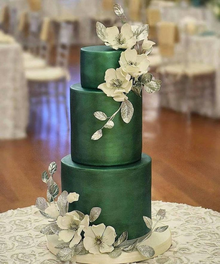 a three tiered green cake with white flowers on the top and side, sitting on a table