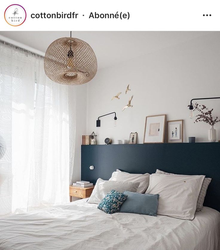 a bed with white linens and blue headboard next to a window in a bedroom