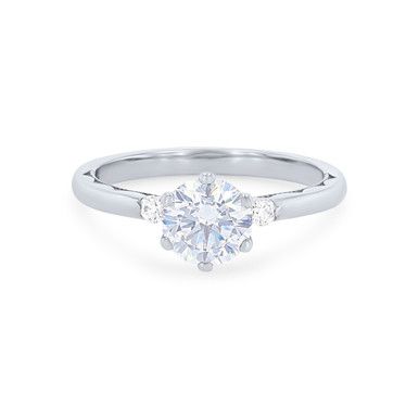 a white gold engagement ring with three stones on the band and a round brilliant diamond center