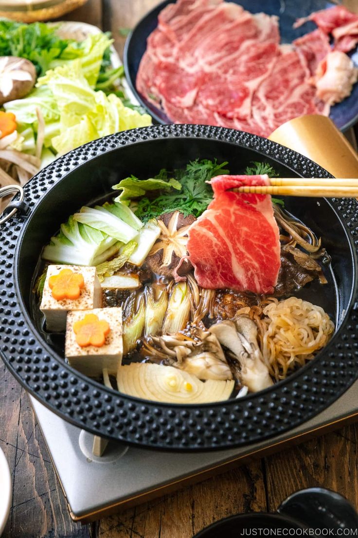 an assortment of food is being prepared on a stove with chopsticks in it