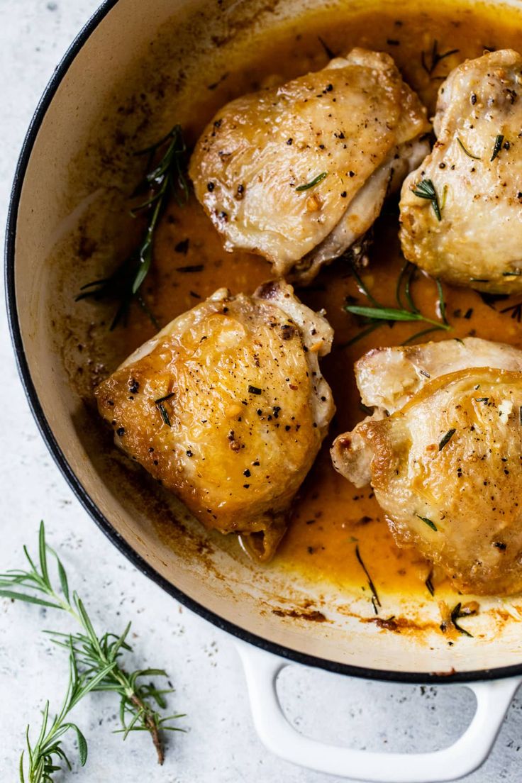 chicken thighs with gravy in a skillet on a white countertop next to fresh herbs