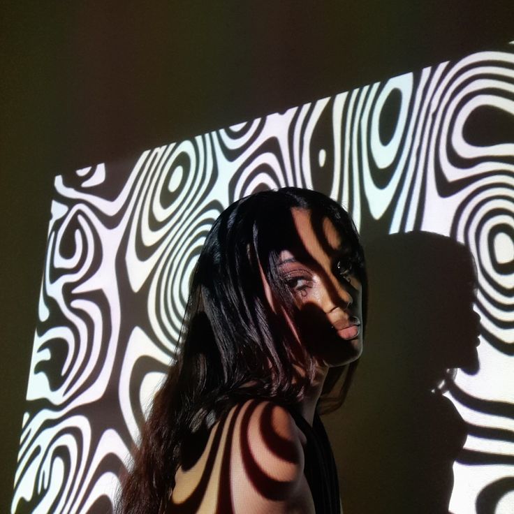 a woman standing in front of a wall with an artistic pattern on it's face