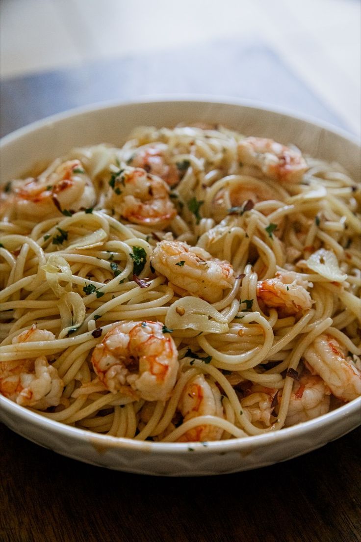 a white bowl filled with pasta and shrimp on top of a wooden table next to a fork