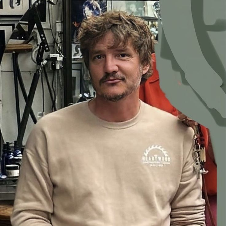 a man in a tan shirt is sitting down and looking at the camera with his hands on his hips