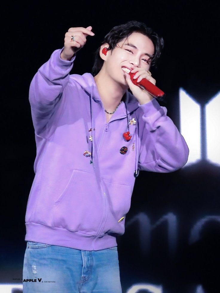 a male in a purple hoodie is holding a red object up to his mouth