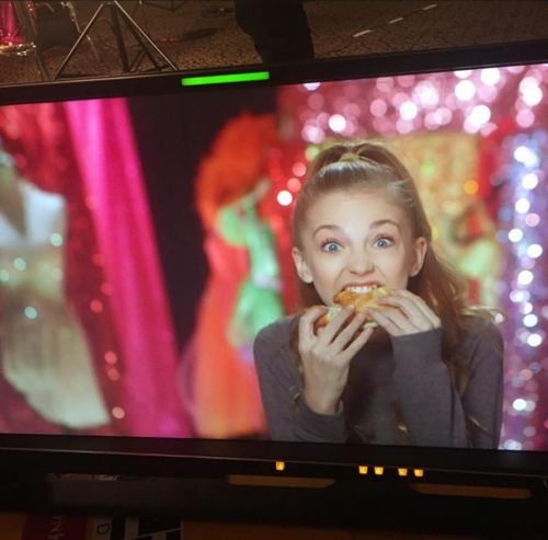 a woman eating a piece of pizza in front of a tv screen with colorful lights behind her