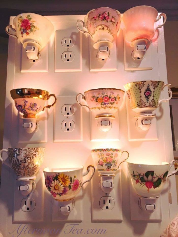 there are many cups and saucers on the shelf with lights in front of them