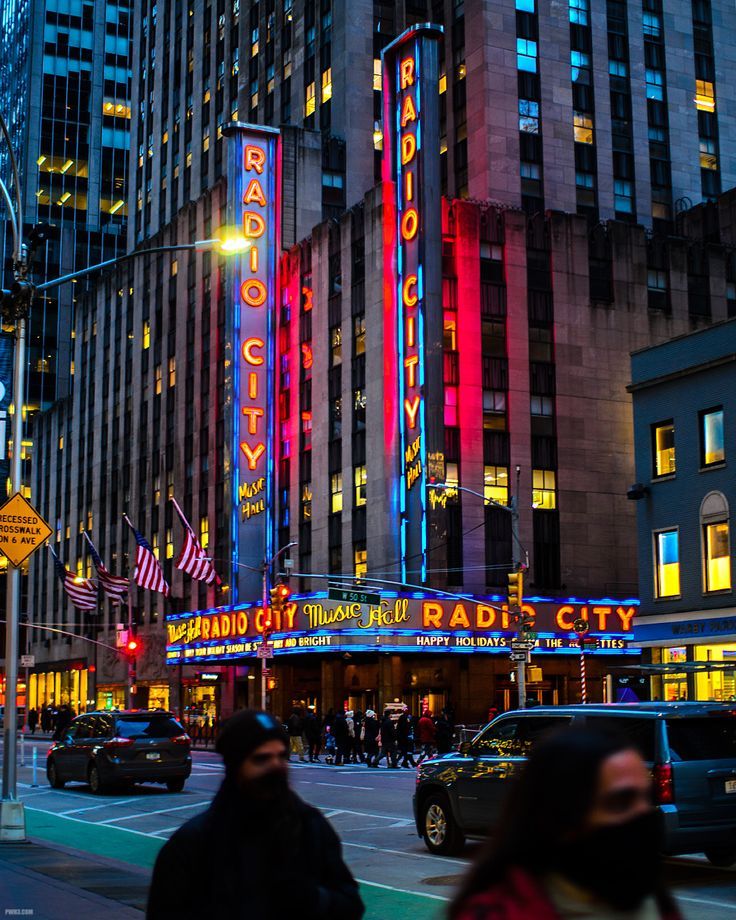 people are walking down the street in front of some tall buildings with neon lights on them